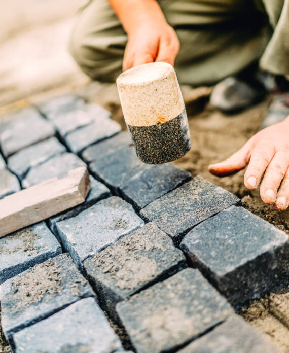 Male construction worker using granite cobblestone blocks to create path or sidewalk